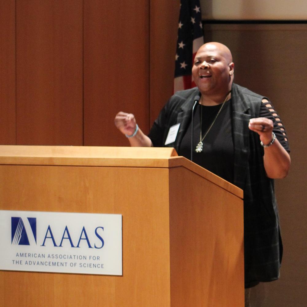 STPF Director Rashada Alexander speaking behind a wooden podium with the AAAS logo on the front.