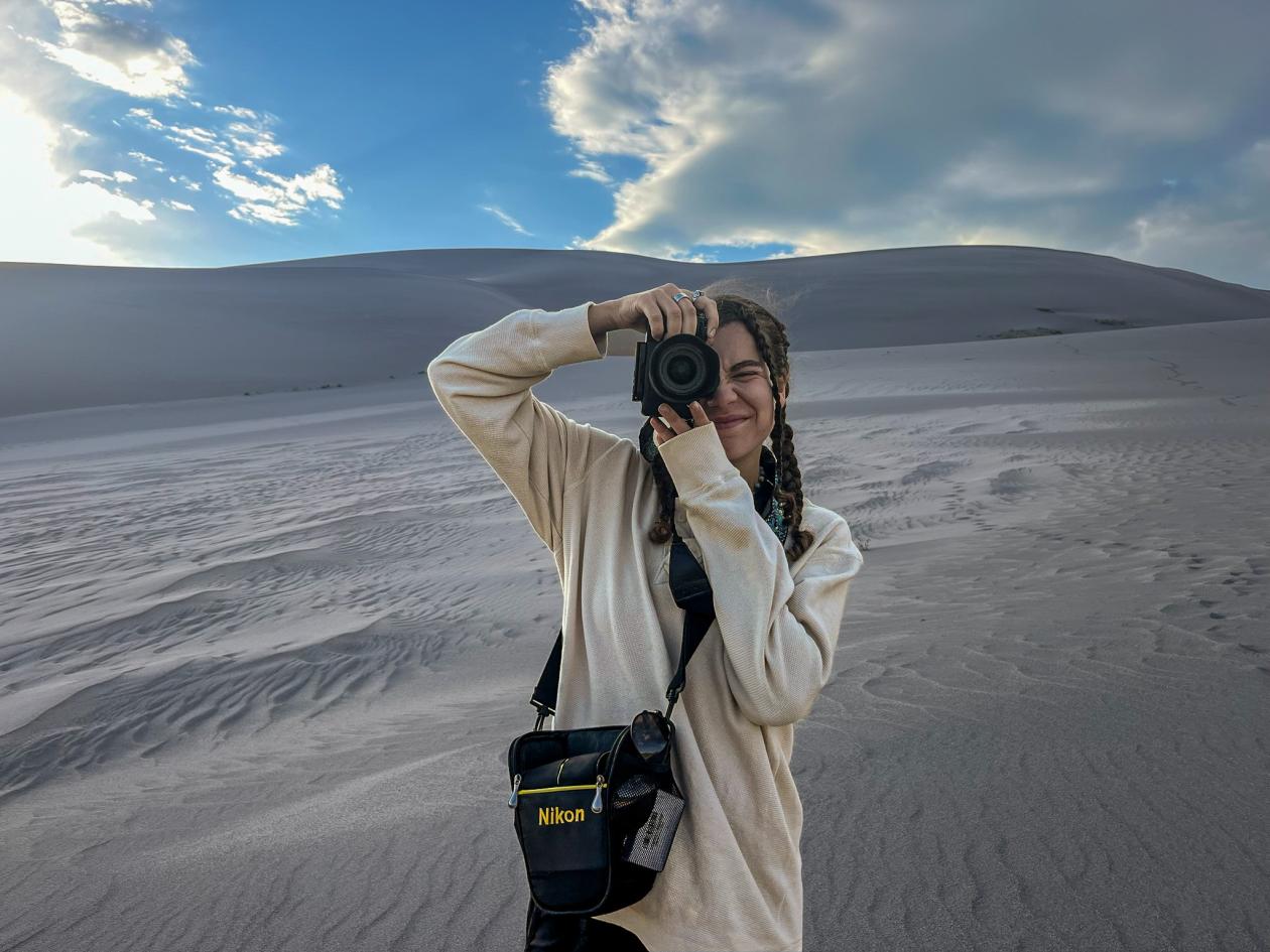 Rachael holding her camera in front of sand dunes.