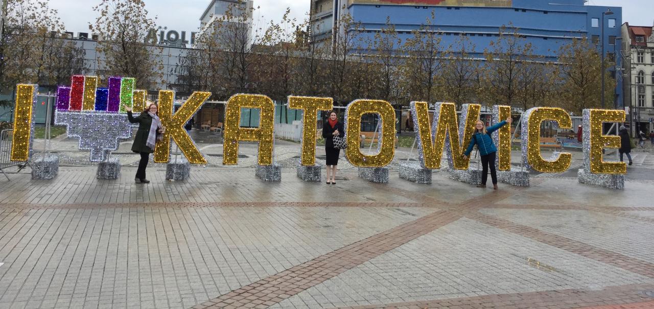 STPF alum fellows in front of a sign of Katowice, Poland. Image by Gillian Bowser (featuring Nycole Scheverria, Shelby Mcclelland and Sarah Whipple)