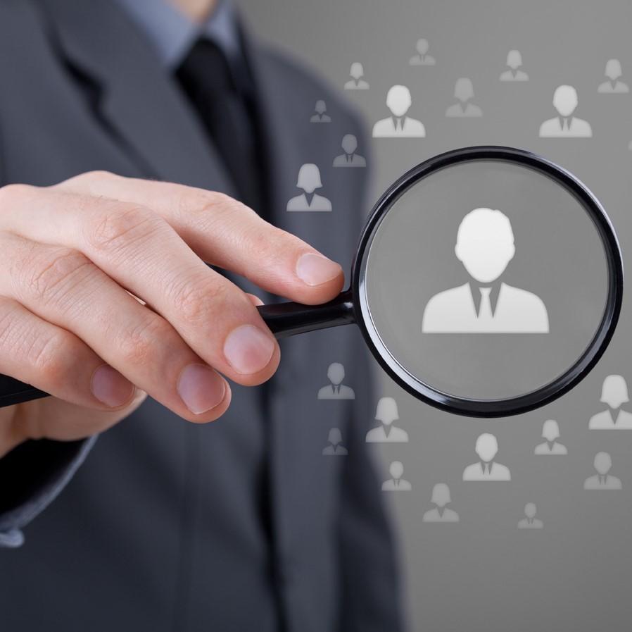 Hand holding a magnifying glass with a white icon of a person in the middle.
