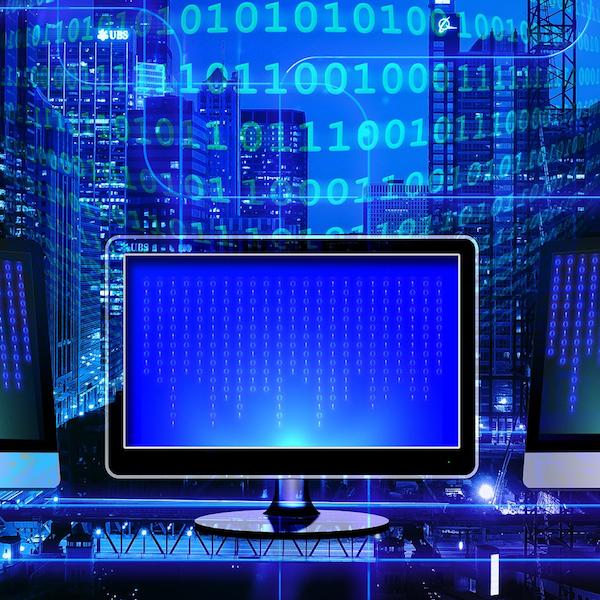 Blue monitor in front of a neon blue wall of binary numbers. By Pixabay.