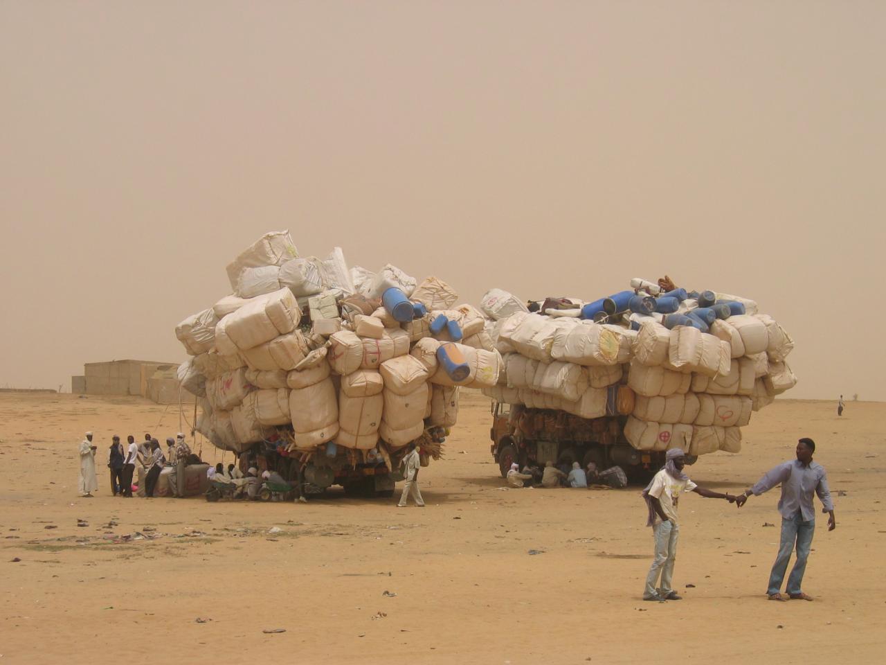 Photograph of people in the desert sitting next to piles of their belongings. By Patrick Christian.