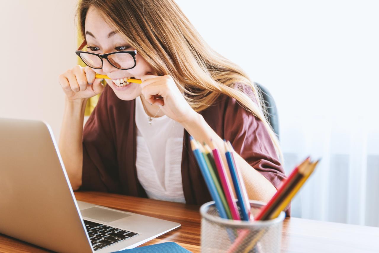 Woman biting a pencil while looking at her laptop, by Unsplash.