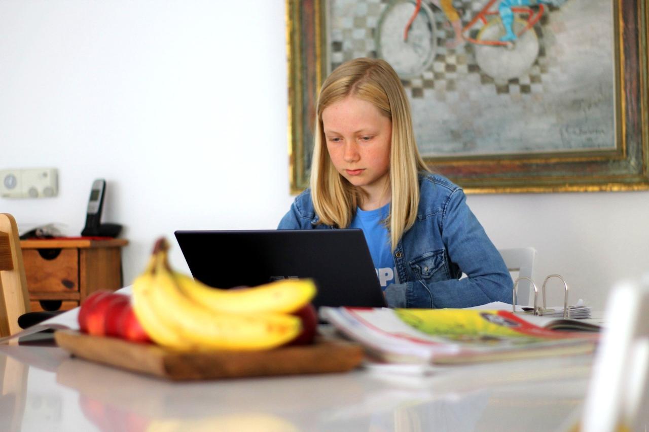 Young girl sitting at home in front of a black laptop.