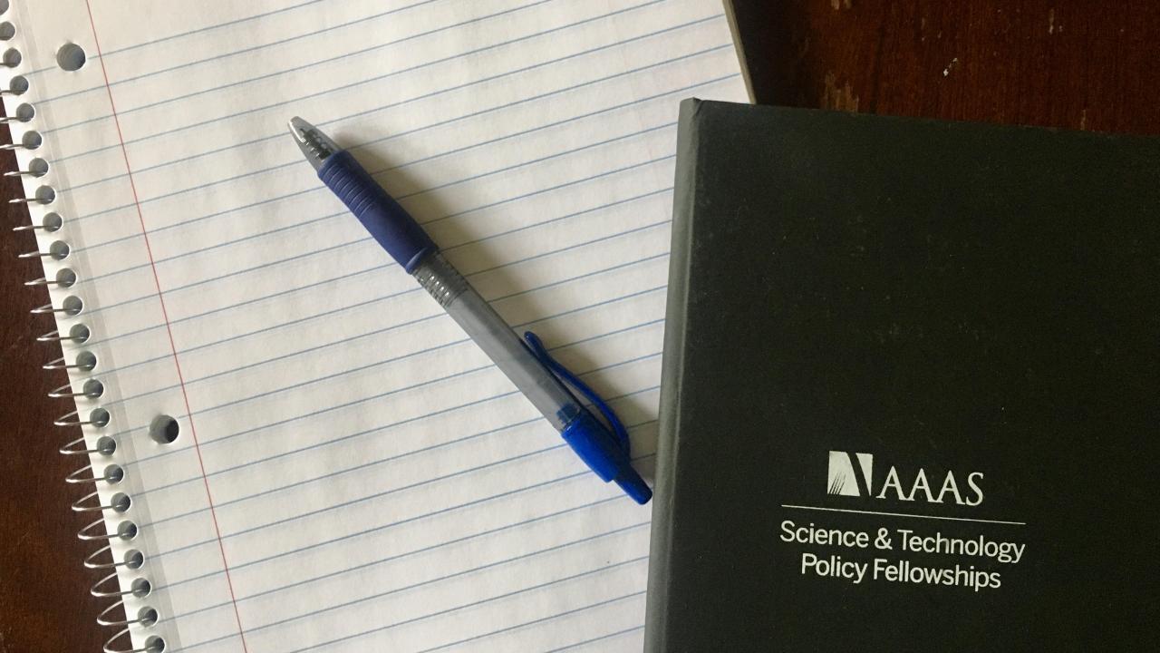 A blank notepad and pen, with an AAAS STPF notebook in the corner
