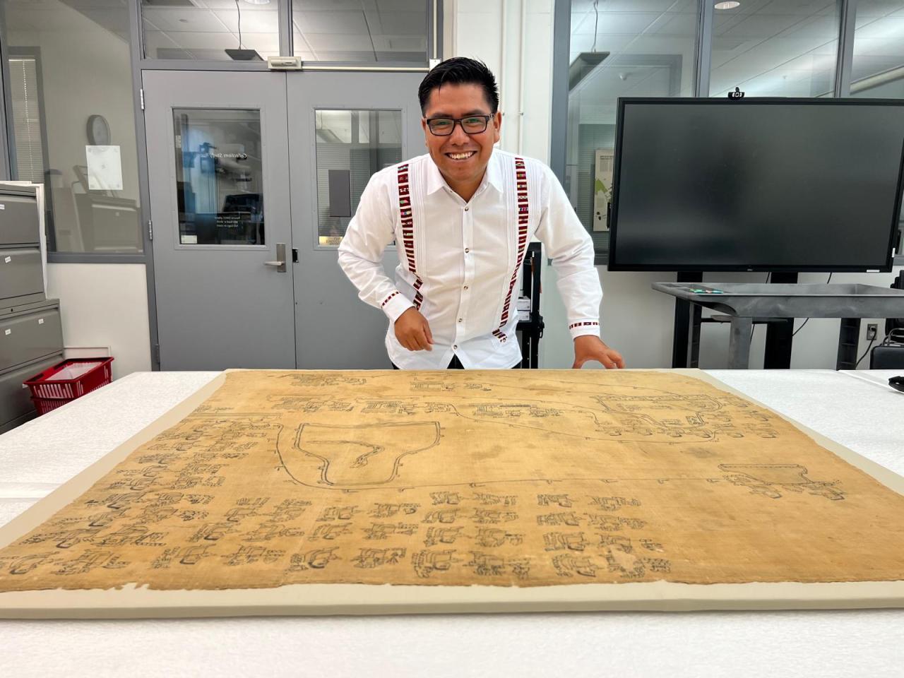 Dr. Omar Aguilar standing over a parchment of Mixtec Codices.