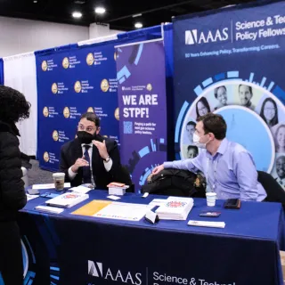 Two men sitting at a table with masks and AAAS in the background