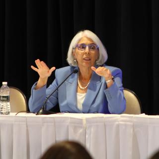Arati Prabhakar, director of the White House Office of Science and Technology Policy and Science Advisor to the President, sitting at a white table and speaking to fellows.