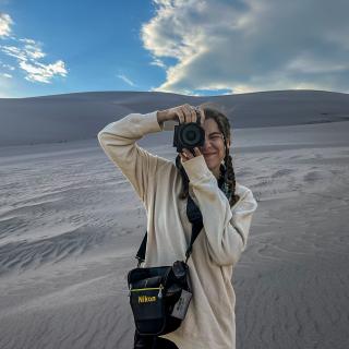 Rachael holding her camera in front of sand dunes.