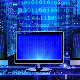 Blue monitor in front of a neon blue wall of binary numbers. By Pixabay.