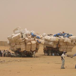 Photograph of people in the desert sitting next to piles of their belongings. By Patrick Christian.