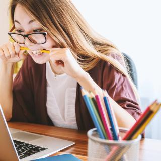Woman biting a pencil while looking at her laptop, by Unsplash.
