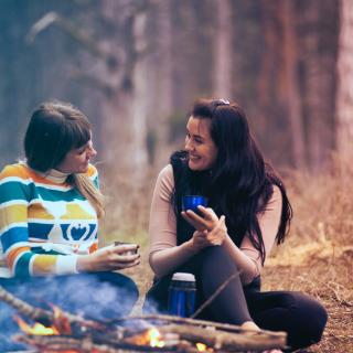 Two girls sitting in front of a bonfire in a forest, by Oleksandr Pidvalnyi, Pexels