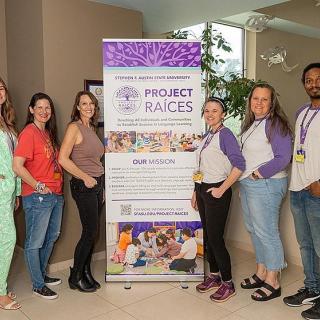 Dr. Chrissy Cross and Dr. Marisol Diaz, and other members of the Project RAICES team, stand in front of a banner